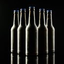 Horizontal image of five dark glass bottles of lager beer with blue crown caps on black background. Drinking alcohol, refreshment and lager day celebration concept. Horizontal image of five dark glass bottles of lager beer with blue crown caps on black background. Drinking alcohol, refreshment and lager day celebration concept.